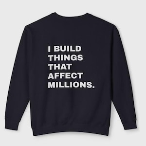 Op de afbeelding: Marineblau sweatshirt met de witte tekst "I BUILD THINGS THAT AFFECT MILLIONS." De trui met lange mouwen en ronde hals heeft een effen kleur en een minimalistisch ontwerp.