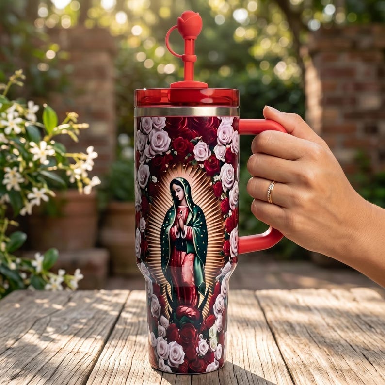 May include: A red and burgundy tumbler with a handle, featuring an image of Our Lady of Guadalupe surrounded by roses. The tumbler has a red lid and a rose-shaped stopper. The tumbler is held by a person.