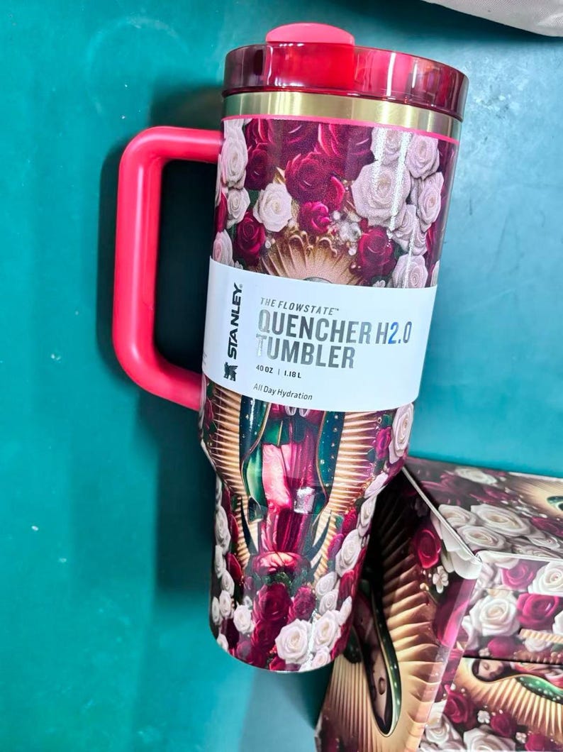 May include: A red and floral Stanley Quencher H2.0 Tumbler with a handle. The tumbler features a design of red and white roses and the text "QUENCHER H2.0 TUMBLER". It holds 40 oz.