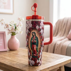 May include: A large red and stainless steel tumbler with a handle and a straw. The tumbler features an image of the Virgin Mary surrounded by roses. The straw has a rose-shaped topper. The tumbler is on a wooden table.