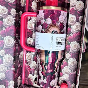 May include: A floral-themed Stanley Quencher tumbler with a red lid and handle, featuring a design of roses in shades of red, pink, and white. The tumbler is packaged in a box with a matching rose pattern. The text on the tumbler reads "The Flowstate Quencher Tumbler".