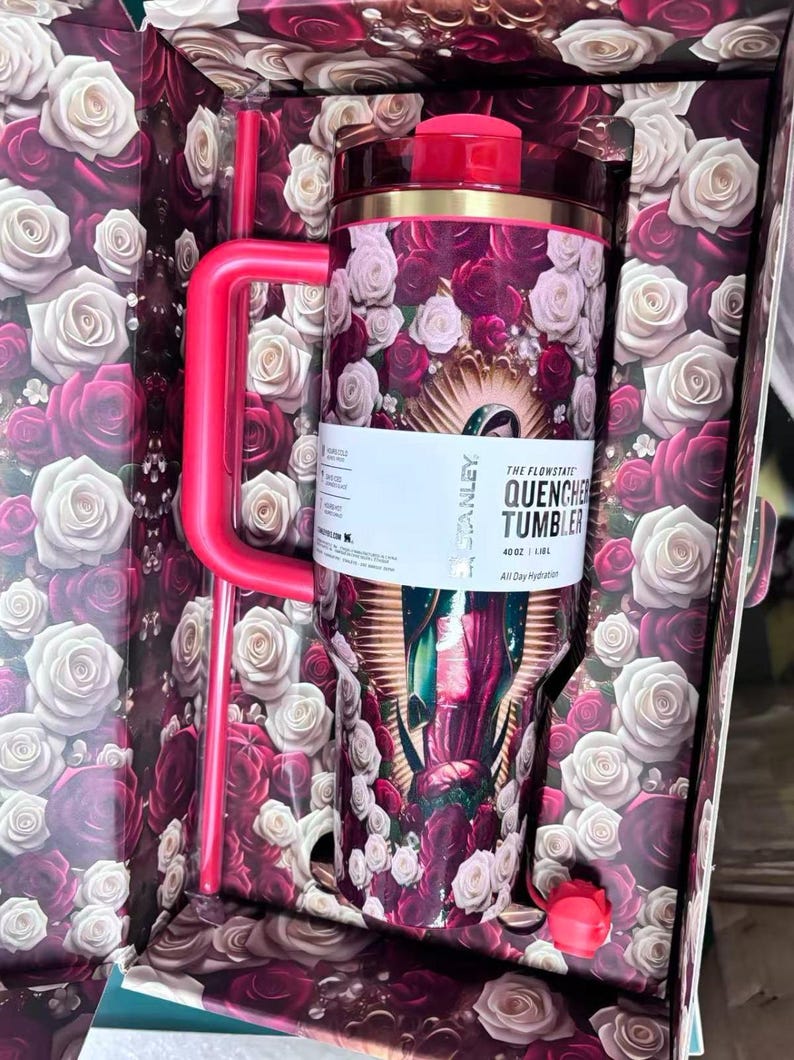 May include: A floral-themed Stanley Quencher tumbler with a red lid and handle, featuring a design of roses in shades of red, pink, and white. The tumbler is packaged in a box with a matching rose pattern. The text on the tumbler reads "The Flowstate Quencher Tumbler".