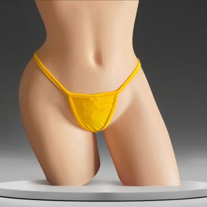 May include: A bright yellow thong bikini bottom featuring a minimalist design with thin side straps and a triangular front panel. The garment is displayed on a neutral mannequin torso, highlighting the solid, vibrant yellow fabric and clean lines.