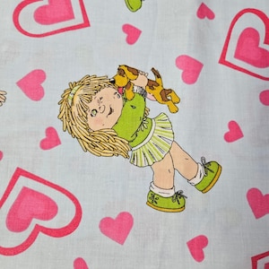 Peut inclure: Un tissu bleu clair avec une illustration de dessin animé d'une fille tenant un chiot. La fille a les cheveux blonds et porte une tenue verte avec des chaussures vertes. Des cœurs roses sont dispersés sur le tissu.