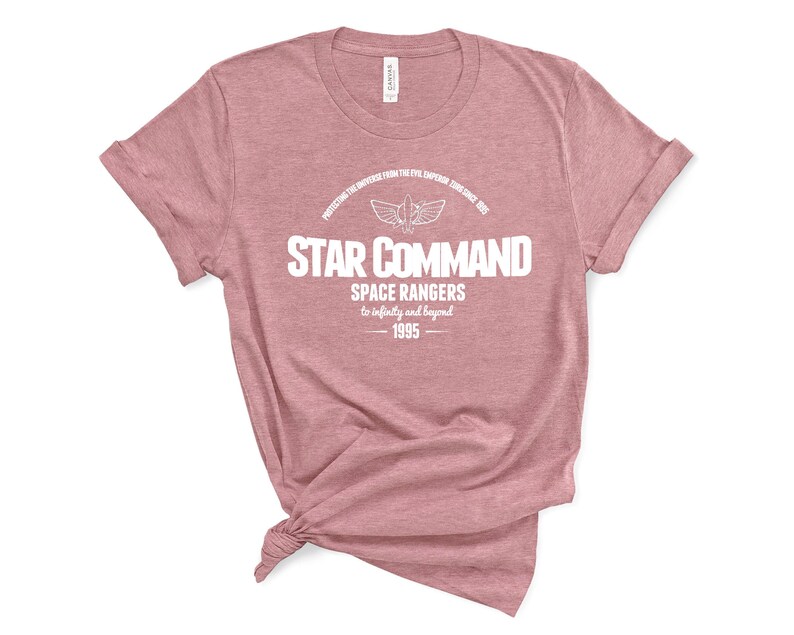Op de afbeelding: Een stoffig roze t-shirt met de witte tekst "STAR COMMAND". De tekst "SPACE RANGERS" en "to infinity and beyond" staan er ook op. Het t-shirt heeft ook het jaartal "1995" erop staan.