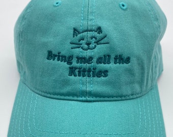 May include: A turquoise blue baseball cap with a black embroidered cat face and the text "Bring me all the kitties".