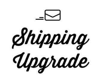 May include: Black and white graphic with the words "Shipping Upgrade" in a cursive font. Above the text is a small envelope icon with lines indicating movement, all on a white background.