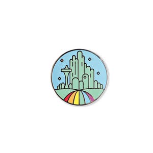 Op de afbeelding: Een ronde emaille pin met een groene skyline van een stad en een regenboogweg die er naartoe leidt. De stad is omringd door een blauwe lucht met witte sterren.