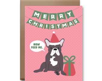 May include: A pink Christmas card with a French bulldog wearing a Santa hat and holding a red gift box. The card has a green banner that says "Merry Christmas" and a speech bubble that says "Now feed me."