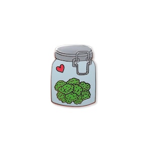 May include: A blue glass jar with a metal lid and a red heart on the side. The jar is filled with green cannabis buds.
