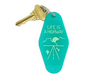 May include: A turquoise blue motel key tag with the text "Life is a Highway" and a graphic of a desert landscape with a road, mountains, a setting sun, and cacti.