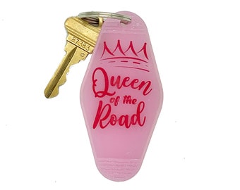 May include: Pink motel key chain with a gold key attached. The keychain has a crown and the text "Queen of the Road" in red.