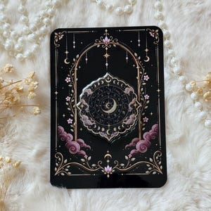Peut inclure: Une broche circulaire présentant un croissant de lune central entouré d'une roue du zodiaque avec des symboles astrologiques, sur un fond noir avec des accents floraux roses, des nuages violets et un motif d'arche orné.