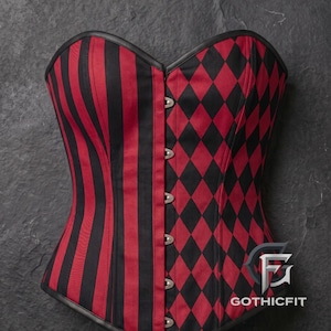 May include: A corset featuring a split design with vertical red and black stripes on one side and a red and black diamond pattern on the other. The garment has a sweetheart neckline, a front busk with metal clasps, and the text GOTHICFIT.