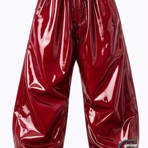 May include: Deep red, high-gloss vinyl joggers featuring a relaxed, baggy fit with an elasticized waistband and matching drawstring. The pants have gathered elastic cuffs at the ankles and a reflective logo with the text GOTHICFIT at the bottom.