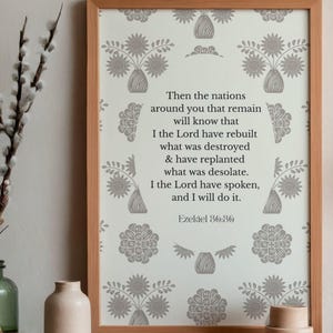 May include: A framed print with a light wood frame. The print features a repeating floral pattern in gray and white, surrounding a central text from Ezekiel 36:36. The text is in a serif font.