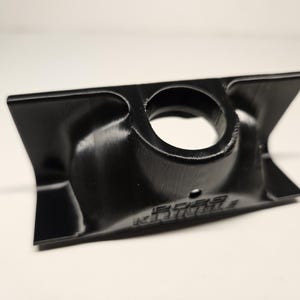 May include: A black, 3D-printed component with a central circular aperture and flared sides. The object has a textured finish, and the text "BOBS" is visible. The design is symmetrical, suggesting it's a functional part or a component.