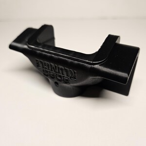 May include: A black, 3D-printed object with the text "2023 KLUNGLE" embossed on its side. The object has a curved design with a rectangular opening on one end and a raised section on the other. The item is likely a custom-made part or accessory.