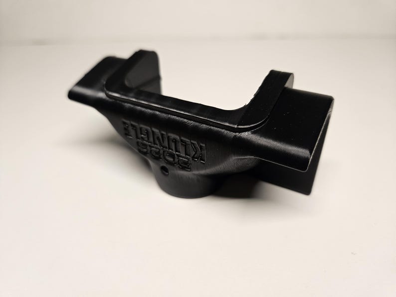 May include: A black, 3D-printed object with the text "2023 KLUNGLE" embossed on its side. The object has a curved design with a rectangular opening on one end and a raised section on the other. The item is likely a custom-made part or accessory.