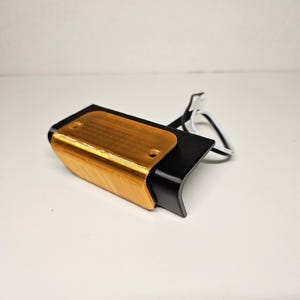 May include: A black and gold-coloured electronic device with a curved design. The top section is gold, while the rest of the device is black. White and black wires extend from the device.