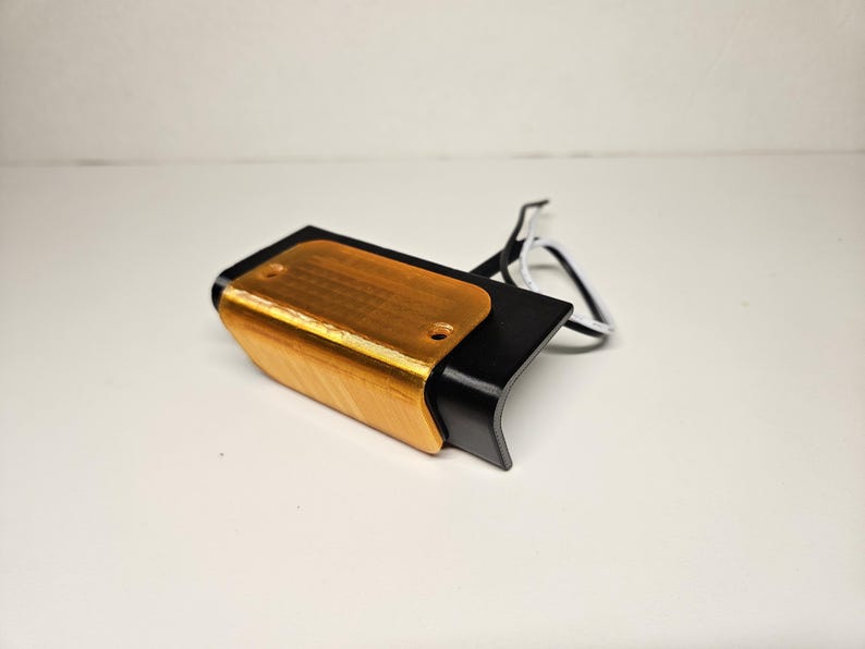 May include: A black and gold-coloured electronic device with a curved design. The top section is gold, while the rest of the device is black. White and black wires extend from the device.