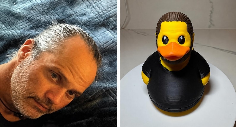 Puede incluir: Un pato de goma amarillo con un peinado casta&ntilde;o moldeado y barba negra, que viste una camiseta negra lisa. El pato tiene un pico naranja brillante y ojos negros, dise&ntilde;ado para parecerse a una persona con vello facial y ropa oscura.