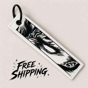 May include: White rectangular keychain with a black illustration of a wolf's eye and part of its face. The keychain has a black metal ring and the text "FREE SHIPPING" in a stylized font.