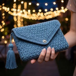 May include: A blue crocheted clutch with a flap closure and a tassel. The clutch features a textured stitch pattern and a silver-toned button clasp. The tassel is attached to the side of the clutch.