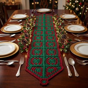 May include: A rectangular crochet table runner featuring a repeating granny square pattern in alternating dark green and deep red yarn. The runner is centered on a dark wood dining table set with white plates, gold chargers, and silverware.