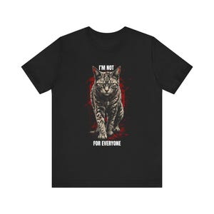 Könnte beinhalten: Schwarzes T-Shirt mit einer detaillierten Illustration einer Katze und dem Text "I'M NOT FOR EVERYONE". Die Katze ist in Grau- und Brauntönen gehalten, mit rotem Hintergrund.
