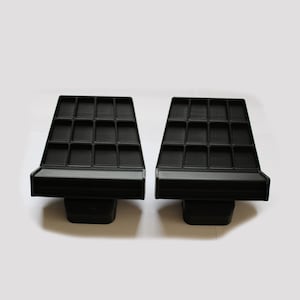 Könnte beinhalten: Zwei schwarze, abgewinkelte Display-Tabletts mit mehreren kleinen Fächern. Jedes Tablett hat eine rechteckige Basis und eine schräge Oberseite mit einem Raster aus rechteckigen Schlitzen. Die Tabletts sind für das Halten und Organisieren kleiner Gegenstände konzipiert.