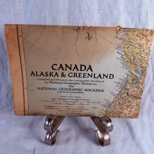 May include: A vintage paper map titled CANADA ALASKA & GREENLAND, compiled by the National Geographic Society. The map features a tan background with black text, a scale of 126.3 miles to the inch, and a detailed cartographic section on the right.