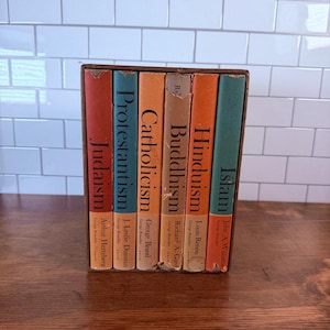 Könnte beinhalten: Ein Set aus sechs gebundenen Büchern in einem braunen Pappschuber. Die Buchrücken sind rot, blau, orange, beige und grün gefärbt und tragen jeweils den Namen einer Weltreligion sowie den Autorennamen in schwarzer Serifenschrift.