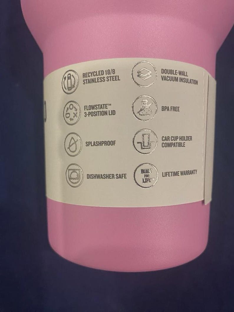 May include: A pink insulated tumbler with a white label. The label includes text that reads "RECYCLED 18/8 STAINLESS STEEL", "FLOWSTATE 3-POSITION LID", "SPLASHPROOF", "DISHWASHER SAFE", "DOUBLE-WALL VACUUM INSULATION", "BPA FREE", "CAR CUP HOLDER COMPATIBLE", and "LIFETIME WARRANTY".