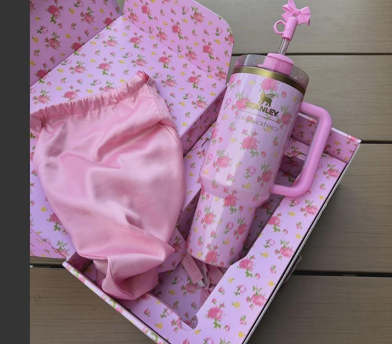 May include: A pink floral Stanley tumbler with a handle and straw, presented in a matching floral box. A pink satin bag is also included. The tumbler features the Stanley logo and the text "Love Shack Fancy".