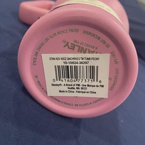 May include: Pink Stanley 400z tumbler with a handle. The bottom of the tumbler features a barcode and product information, including the text "STAN ADV 400Z QNCHRH2.0 TM TUMB PEONY". The tumbler is BPA free and dishwasher safe.