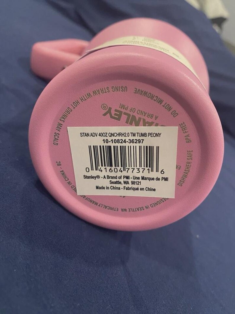May include: Pink Stanley 400z tumbler with a handle. The bottom of the tumbler features a barcode and product information, including the text "STAN ADV 400Z QNCHRH2.0 TM TUMB PEONY". The tumbler is BPA free and dishwasher safe.