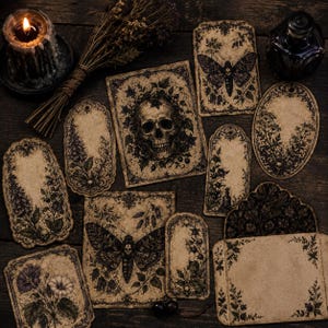 May include: A collection of vintage-style paper tags and cards featuring dark botanical illustrations, moths, and a skull. The set includes various shapes with intricate black ink designs on aged, tan-colored paper, arranged with a candle and dried herbs.