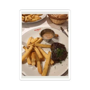 May include: A plate of food featuring a grilled steak, golden french fries, and a small metal cup of sauce. The plate has the word "Bouillon" printed on it. A basket of bread is in the background.