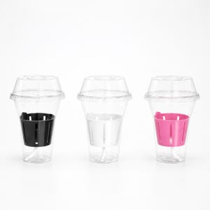 May include: Three clear plastic cups with dome lids, each containing a slotted inner basket. The left cup has a black basket, the center cup has a white basket, and the right cup has a bright pink basket. These containers are arranged in a row.