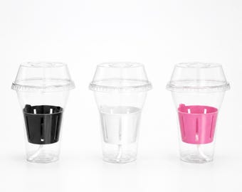 May include: Three clear plastic cups with dome lids, each containing a slotted inner basket. The left cup has a black basket, the center cup has a white basket, and the right cup has a bright pink basket. These containers are arranged in a row.