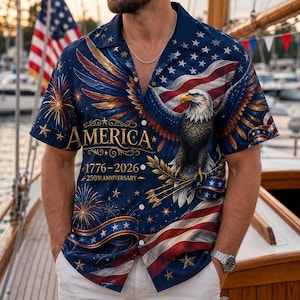 Puede incluir: Camisa abotonada azul marino con un diseño patriótico. Presenta una bandera estadounidense, un águila con las alas extendidas y la palabra "AMERICA" con el texto "1776-2026 250th Anniversary". La camisa tiene cuello clásico y mangas cortas.