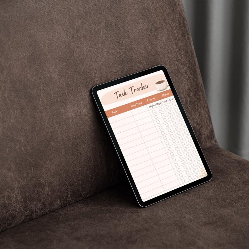 May include: A digital tablet displaying a "Task Tracker" template with a coffee cup graphic. The screen features columns for tasks, due dates, priority, and status. The tablet is set against a brown leather background.