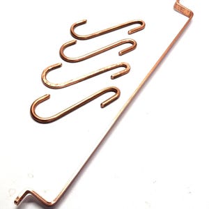 May include: A set of four copper S-hooks and one long, straight copper rod with bent ends. The metal components have a smooth, metallic finish and a distinct reddish-brown copper color. The hooks are curved at both ends for hanging purposes.