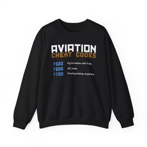 Puede incluir: Sudadera negra con texto blanco y naranja "AVIATION CHEAT CODES". Debajo, los números 7500, 7600 y 7700, cada uno con una instrucción de aviación.