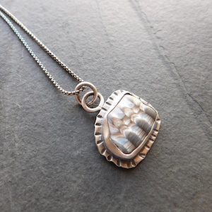 May include: A silver necklace with a textured, silver pendant. The pendant has a geometric shape and a textured surface.