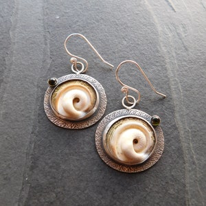 May include: A pair of silver earrings with a circular design. Each earring features a white spiral shape surrounded by a gold band and a small green gemstone.