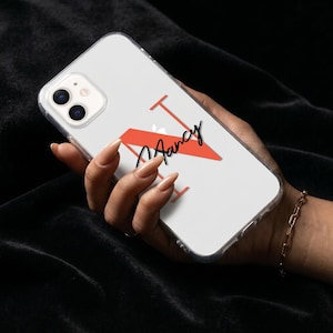 May include: Clear phone case with a red letter "N" and the name "Nancy" in black script. The phone case is held in a hand against a black background. The phone has a dual-lens camera.