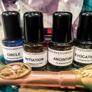 May include: Four small glass bottles with black caps and white labels, each labeled Ceridwen's Handblended with the names Circle, Initiation, Anointing, and Evocation, and the text For External Use Only, positioned behind a copper-colored metal rod.