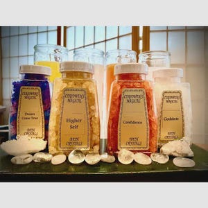 May include: Four clear plastic jars filled with colored bath crystals, each featuring a gold label with the text Ceridwen's Magical. The labels are labeled Dream Come True in blue, Higher Self in yellow, Confidence in orange, and Goddess in white.